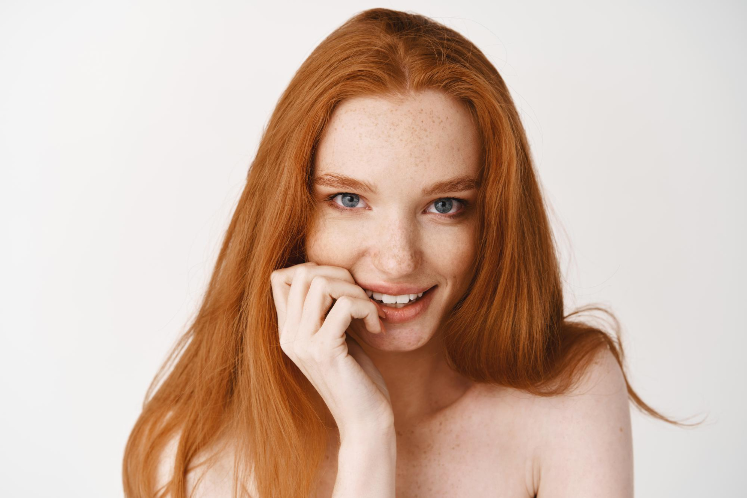close up flirty redhead woman with pale skin no makeup biting fingernail staring front tempted standing white wall naked 1